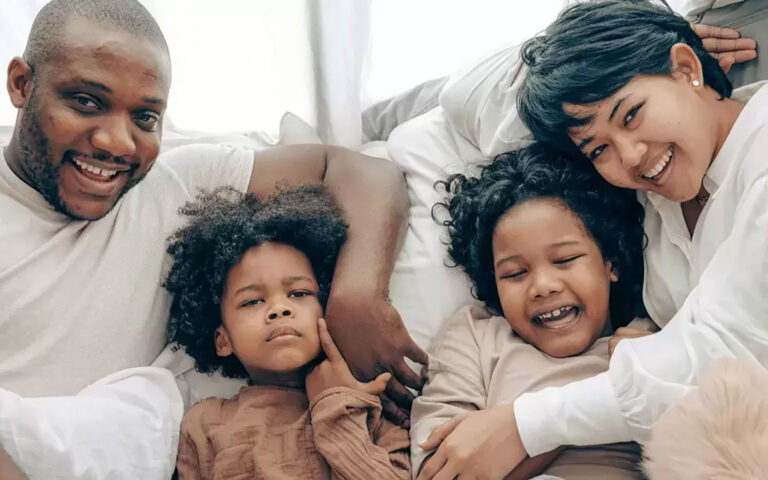 two parents sit on couch cuddling with two children