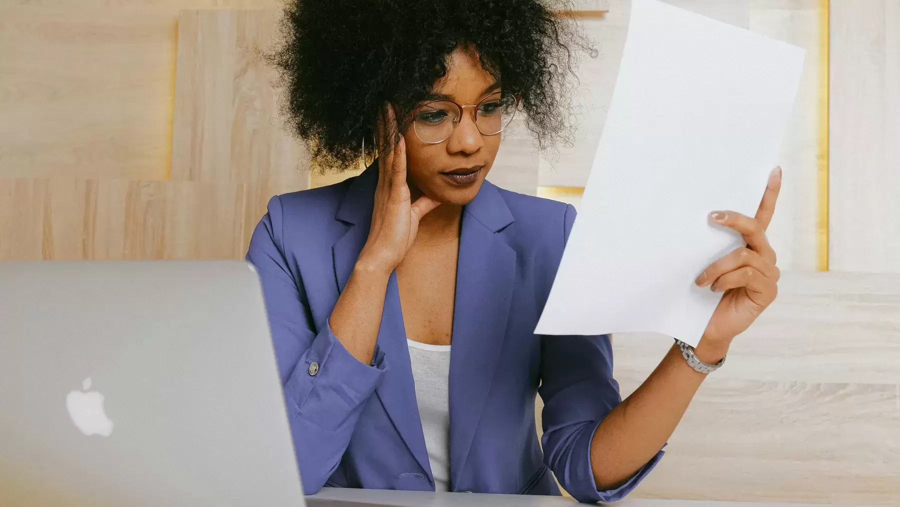 person looks stressed while sitting in front of computer and looking at piece of paper