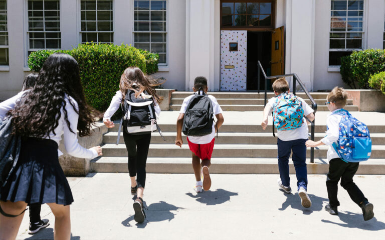 Children wearing backpacks run toward school