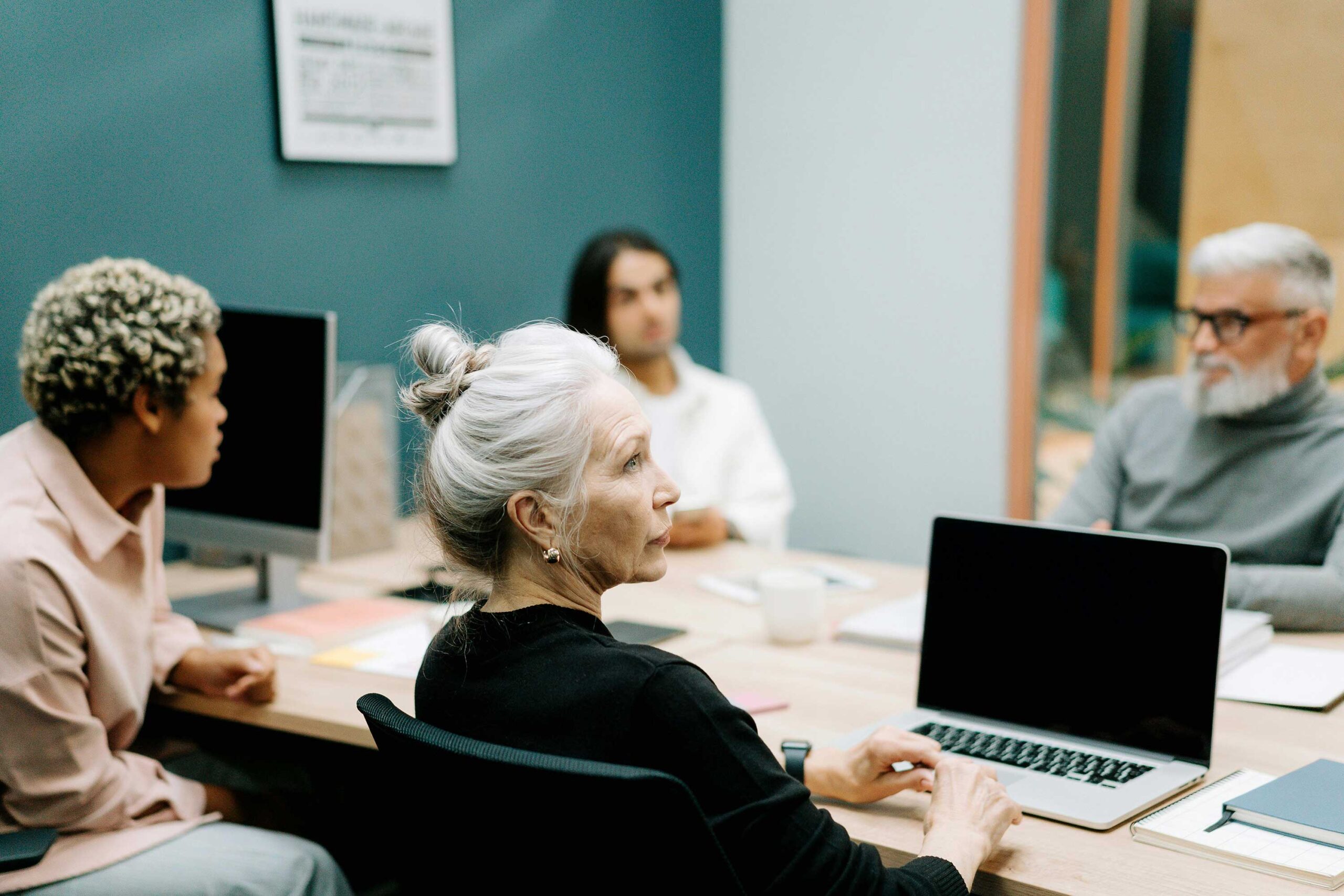 people sit around conference room table, some with laptops open in front of them