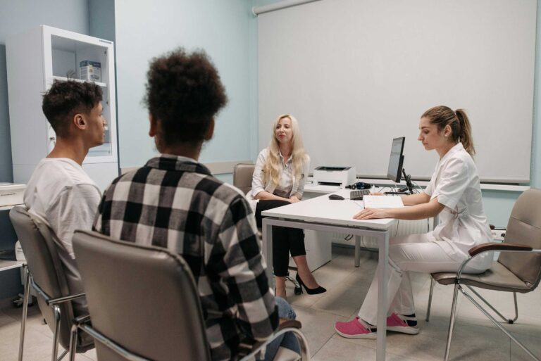 two people sit beside a table while two more people at the table look over paperwork
