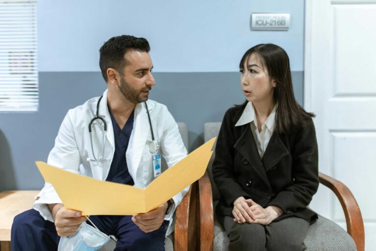 person in doctor's coat talks to another person sitting next to them