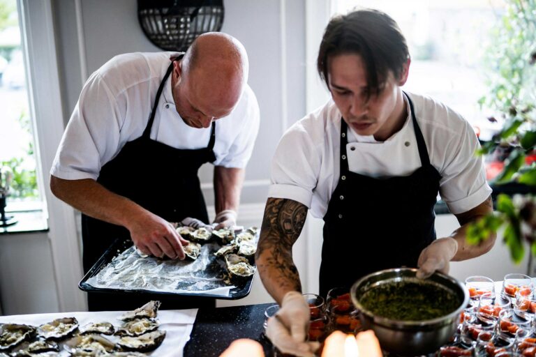 two people prepare food wearing black aprons